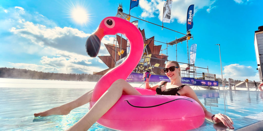 Nainen aurinkolaseissa kelluu pinkin flamingo-uimalelun kanssa altaassa.